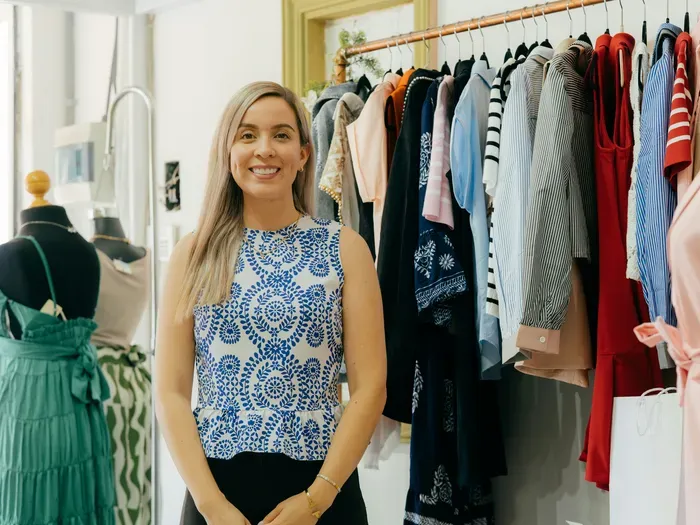 Smiling boutique owner standing in front of colorful clothing rack representing local business community on townservicelist.com